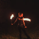 a photo of a woman spinning cathedral fire poi at night, facing away from the camera